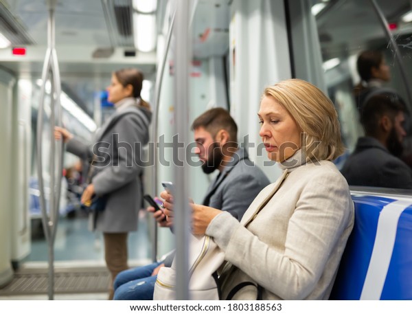 Modern middle aged woman traveling in metro car\
and using mobile phone..