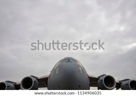 Modern military cargo jet, low and symmetrical in frame with cloudy sky, negative space