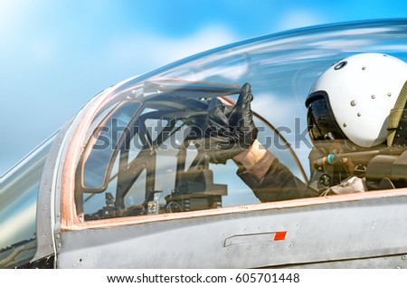 Modern military fighter jet aircraft canopy exterior close up silhouette view pilot waving OK gesture inside cockpit interior airplane parts sky glass reflection aviation aerial panoramic background
