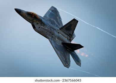 A modern military jet fighter aircraft gliding through an azure sky, producing a white trail of smoke from its engines - Powered by Shutterstock