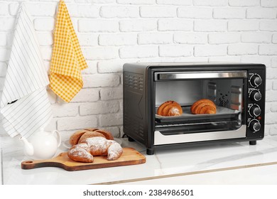 Pequeño horno eléctrico moderno con croissants recién horneados en la cocina