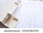 A modern miniature architectural model resembling a house sits atop detailed floor plans, illustrating design and creativity in architecture and building planning.