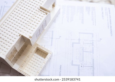 A modern miniature architectural model resembling a house sits atop detailed floor plans, illustrating design and creativity in architecture and building planning. - Powered by Shutterstock