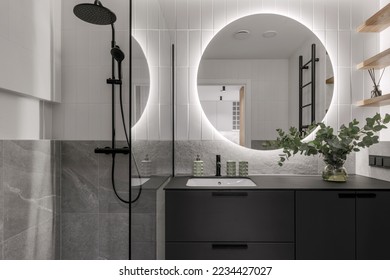Modern minimalistic bathroom interior design with grey stone tiles, black furniture, eucalyptus in glass vase, round mirror.  Aesthetic simple interior design concept.