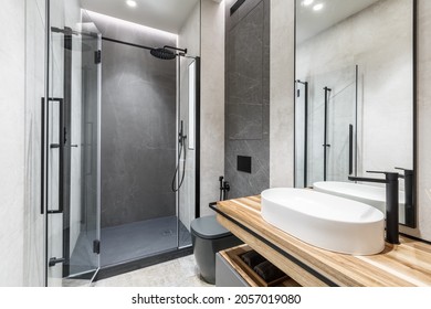 Modernes, helles Badezimmer mit Holzmöbeln, grauen und beigen Steinfliesen und Glasdusche. Innendesign-Konzept 
