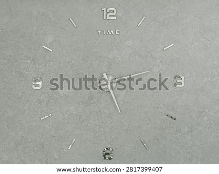Modern mirror wall clock with text time on gray plaster wall surface view.