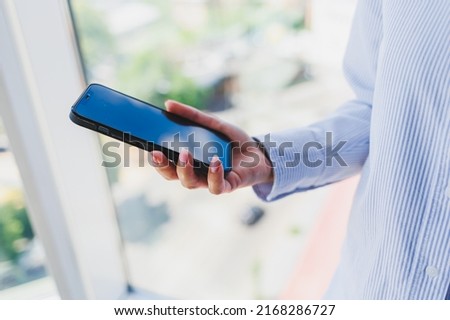 A modern mobile phone with a black screen is held in the hands of a woman, female hands with a smartphone close-up