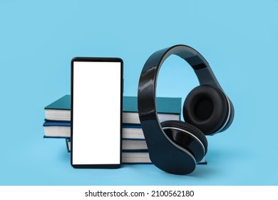 Modern mobile phone, headphones and books on blue background