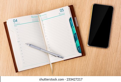 Modern Mobile Phone And Year Business Project Planner Book With Pen On Wood Table