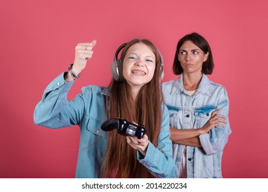 Modern Mom And Daughter In Denim Jackets On Terracotta Background Girl In Headphones Play Game On Phone And Disappointed Angry Mom Stands By