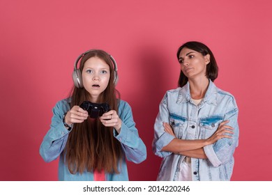 Modern Mom And Daughter In Denim Jackets On Terracotta Background Girl In Headphones Play Game On Phone And Disappointed Angry Mom Stands By