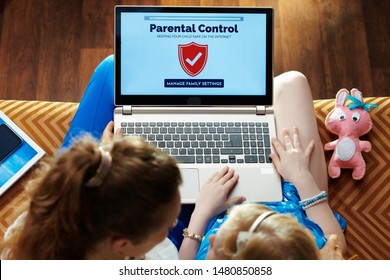 modern mother and daughter sitting on sofa in the modern living room setting up parental control on a laptop.
