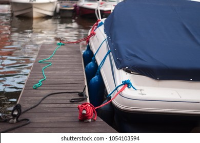 A Modern Motor Boat Windshield And Bow Deck Covered In A Blue Canvas Rain Cover, With A Weathered Wood Dock And Blurry Port In Background