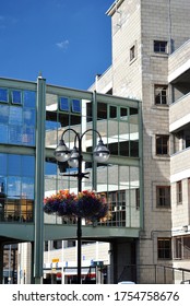 Modern Multi Level Car Park With Reflective Glass Footbridge & Foreground Hanging Baskets 