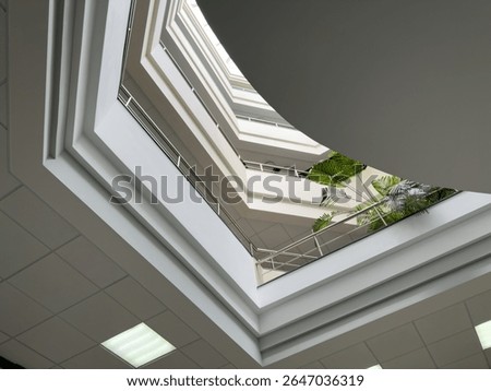 Modern multi level office atrium with geometric architectural lines, white ceilings, glass railings, and tropical plants creating bright and spacious business interior