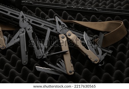 Modern multitool with many tools. A portable multi-tasking military tool lies next to the weapon. Dark background.