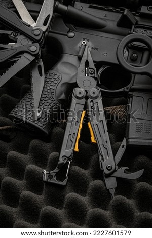 Modern multitool with many tools. A portable multi-tasking military tool lies next to the weapon. Dark background.