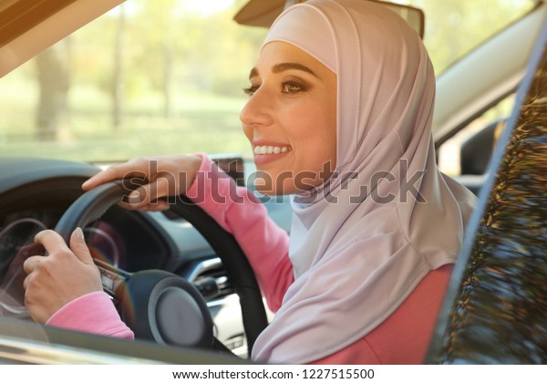 Modern Muslim woman in\
hijab driving car
