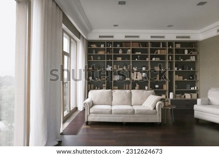 Modern new decorated empty living room with traditional pale sofa, white soft comfortable furniture, large window, bookshelves. Stylish home interior design for city apartment, flat, house