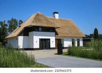 Modern new detached family house with white facade and traditional thatched roof, spacious driveway in rural setting - Netherlands (focus on center of house)