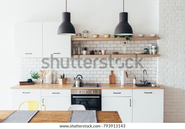 Modern new light interior of kitchen with white\
furniture and dining\
table.