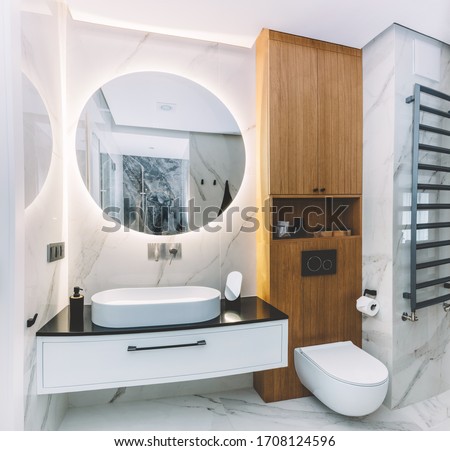 Modern new luxury bathroom. Interior design with marble, wood and stainless steel. Round mirror with led light behind