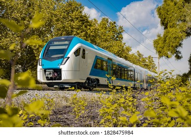 Modern and new passenger commuter Train in white and blue color is traveling on a single track railway line between the green leaves on an autumn day. - Shutterstock ID 1828475984
