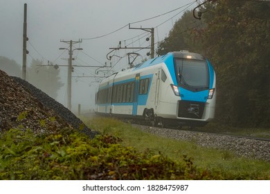 Modern and new passenger commuter Train in white and blue color is traveling on a single track railway line between the green leaves on a cold foggy day. - Shutterstock ID 1828475987