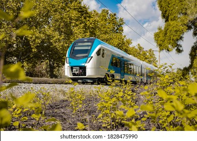 Modern and new passenger commuter Train in white and blue color is traveling on a single track railway line between the green leaves on an autumn day. - Shutterstock ID 1828475990