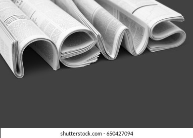 Modern newspapers are folded and composing together the word NEWS, isolated over dark gray background. Concept of business news, news media, print media and mass media at all. Copy space for your text
