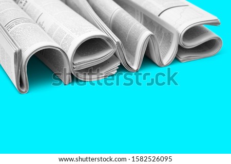 Modern newspapers are folded and composing together the word NEWS, isolated over colored background. Concept of business news, news media, print media and mass media at all. Copy space for your text