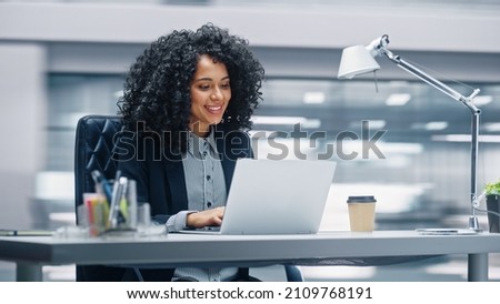Modern Office: Black Businesswoman Sitting at Her Desk Working on a Laptop Computer. Smiling Successful African American Woman working with Big Data e-Commerce. Motion Blur Background
