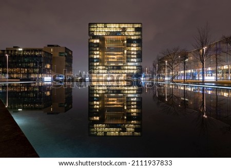 Modern office buildings with perfect reflection in artifical pool and colorful illumination on misty winters night in Essen Ruhr Basin Germany, symmetrical wide angle perspective.