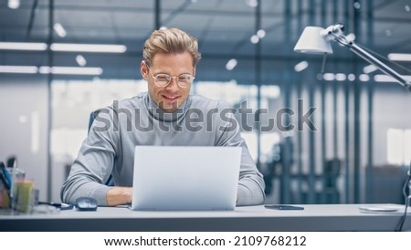 Modern Modern Office: Businessman Sitting at His Desk Working on a Laptop Computer. Digital Entrepreneur working with Big Data e-Commerce Project, Successful Startup. Blurred Background.