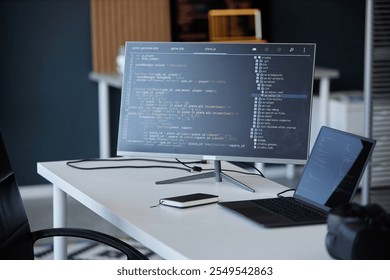 Modern office with a coding interface shown on a monitor, accompanied by a laptop and smartphone, showcasing various technology tools and gadgets in workspace