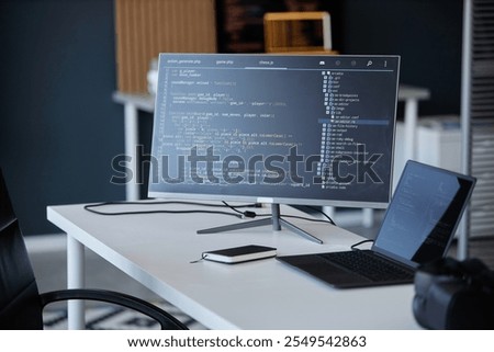 Modern office with a coding interface shown on a monitor, accompanied by a laptop and smartphone, showcasing various technology tools and gadgets in workspace