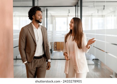 In a modern office corridor, an African-American businessman and his colleague are engaged in a lively discussion, walking together - Powered by Shutterstock