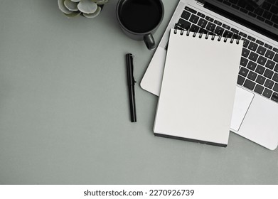 Modern office desk workspace top view with laptop, pen, coffee cup, decor plant, blank spiral notepad and space on grey background. - Powered by Shutterstock