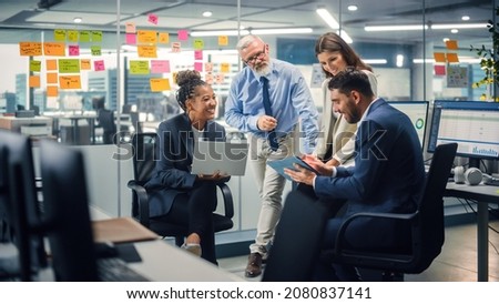 In Modern Office: Diverse Team of Managers Use Laptop and Tablet Computers at a Company Meeting Discussing Business Projects. Young, Motivated and Experienced Employees Brainstorm in Conference Room.