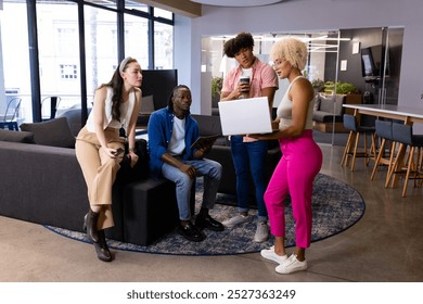 In modern office, diverse young team discussing work. Blue background frames African American man, biracial woman in pink pants, and a Caucasian woman in beige suit. Biracial man with curly hair - Powered by Shutterstock