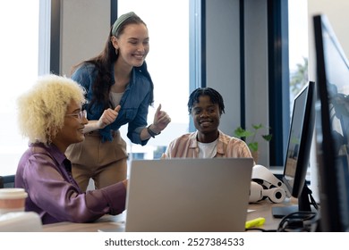 In modern office, diverse young team sharing ideas at computers. Biracial woman with long hair, African American man with twists, and Caucasian woman with ponytail, all dressed casually, unaltered - Powered by Shutterstock