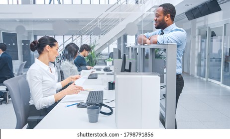 In Modern Office: Handsome Black Manager Flirts With Beautiful Female Business Specialists Working On Her Desk. He Leans On Cubicle Wall And Talks To Her. Young Business People In Open Office.