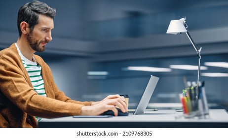 Modern Office: Handsome Businessman Sitting at His Desk Working on a Laptop Computer. Man working with Big Data e-Commerce Analysis. Motion Blur Background Showing Active Work Day.