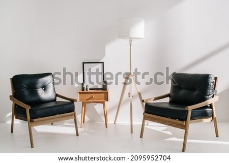 Modern office interior design. Leather armchairs standing near side table with decor and mockup art on picture frame. Flooring lamp and comfortable furniture in waiting room at business center