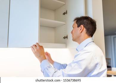 Modern Office Kitchen Room In Building With Young Man Opening Empty Shelf Cabinet Looking Inside Wearing Dress Shirt