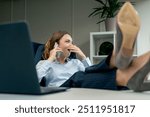 in a modern office with a large window a beautiful worker in a blue shirt sits with her feet on the table allows herself to go too far plays the fool low productivity calling