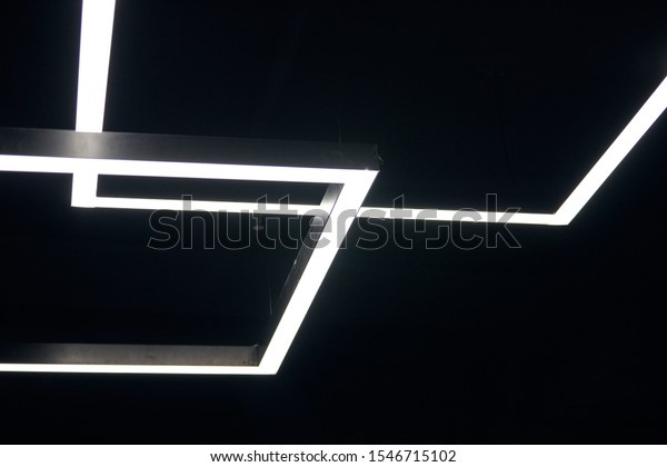 Modern office lighting. Thin lamps\
in office dark ceiling. LED white cold light over\
workplaces.