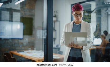 Modern Office: Portrait Of Beautiful Authentic Specialist With Short Pink Hair Standing, Holding Laptop Computer, Concentrated On Her Work. Working On Design, Data Analysis, Plan Strategy