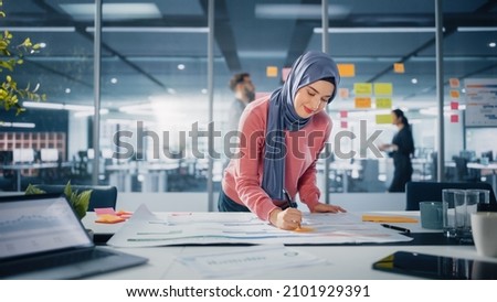 Modern Office: Portrait of Muslim Businesswoman Wearing Hijab Works on Engineering Project, Does Document and Blueprints Analysis. Empowered Digital Entrepreneur Works on e-Commerce Startup Project
