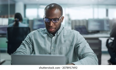 Modern Office: Portrait Of Thoughtful Black IT Programmer Working On Laptop, Finding Solution, Solving Problems, Brainstorming. Male Software Engineer Wearing Glasses Develop App, Program, Video Game